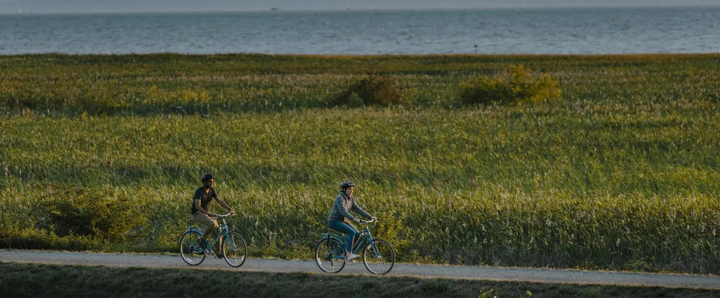 Two cyclists riding the West Dyke Trail along the Richmond waterfront at golden hour